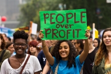 A young woman holds a People over Profit banner at a demonstration