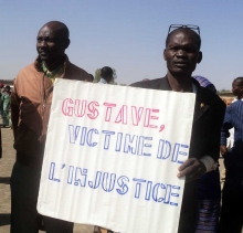 Deux hommes portant un notice "Gustave, victime de l'injustice"